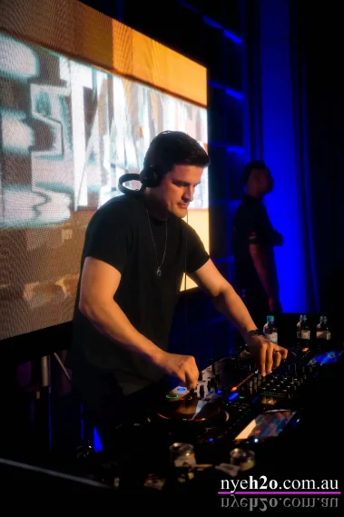 DJ performing on stage at a Melbourne New Year’s Eve event, mixing music on professional equipment with stage lighting and LED screen backdrop
